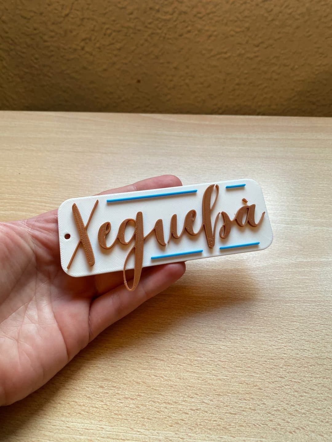 Letras color cobre en relieve sobre una placa blanca, con una fina línea azul