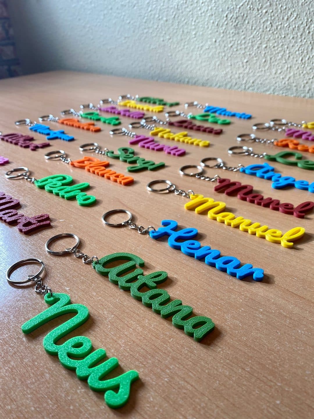 Llaveros de colores con nombres en cursiva sobre una mesa de madera